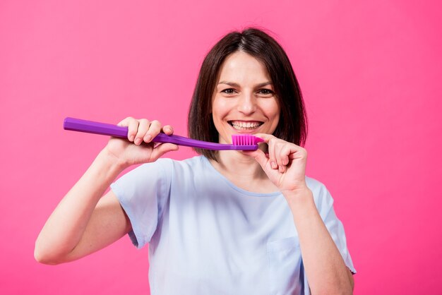 Belle jeune femme heureuse avec une grosse brosse à dents sur fond rose blanc