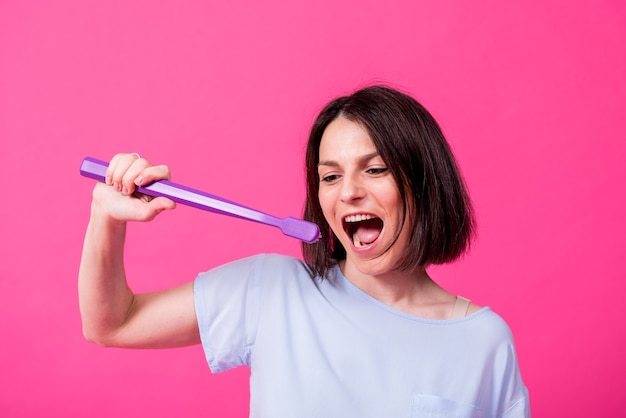 Belle jeune femme heureuse avec une grosse brosse à dents sur fond rose blanc