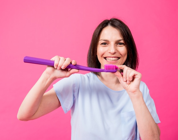 Belle jeune femme heureuse avec une grosse brosse à dents sur fond rose blanc