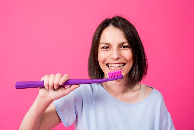 Belle jeune femme heureuse avec une grosse brosse à dents sur fond rose blanc