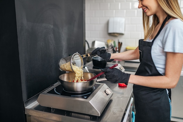 Belle jeune femme heureuse préparant des pâtes avec des sous de tomate pour le dîner.