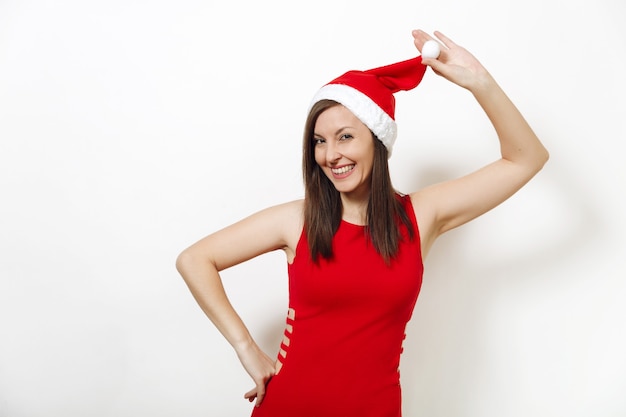 La belle jeune femme heureuse de race blanche avec une peau saine et un sourire charmant portant une robe rouge tenant un chapeau de Noël sur fond blanc. Portrait isolé de Santa girl. Concept de vacances de nouvel an 2018