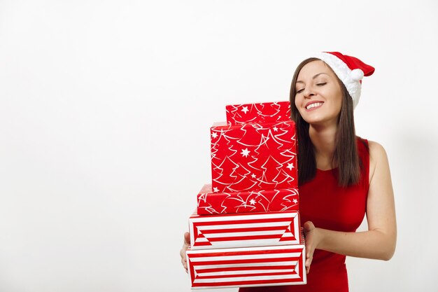 Belle jeune femme heureuse de race blanche avec un sourire charmant vêtue d'une robe rouge et d'un chapeau de Noël tenant des coffrets cadeaux sur fond blanc. Fille de Santa avec présent isolé. Concept de vacances de nouvel an 2018