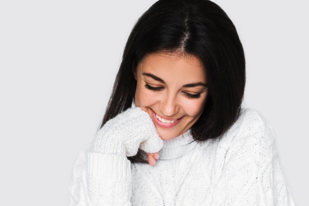 Belle jeune femme heureuse riant sincèrement avec des dents parfaites en pull blanc sur fond gris clair Jolie brune souriante femme studio portrait