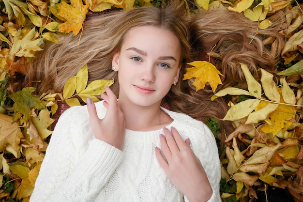 Belle jeune femme heureuse s'amusant avec des feuilles dans le parc