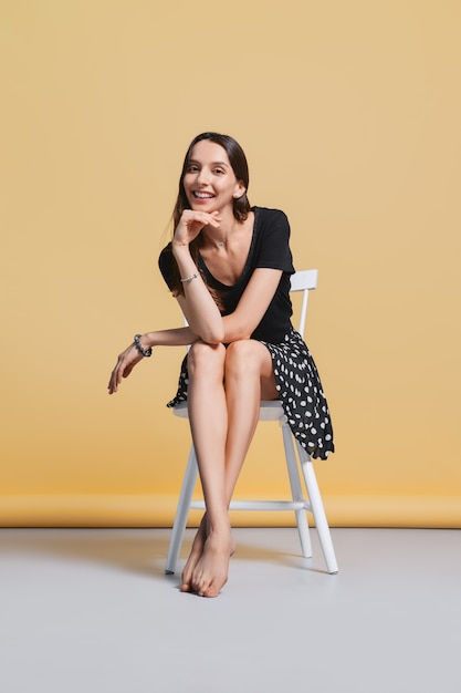 Belle jeune femme heureuse sans maquillage est assise sur une chaise en studio sur jaune
