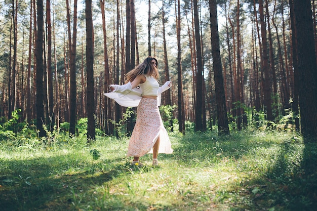 Une belle jeune femme hippie se promène dans la forêt d'été, rit, danse et profite de la vie et de la nature