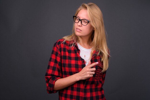 Belle jeune femme hipster aux cheveux blonds portant des lunettes contre le mur gris