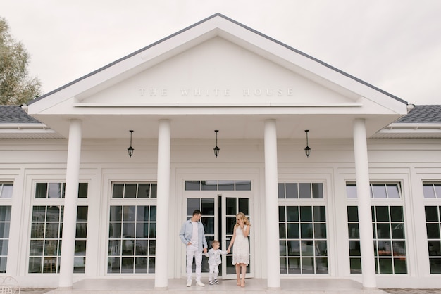 Belle jeune femme homme de famille et son fils dans des vêtements intelligents sur le fond d'une luxueuse maison blanche