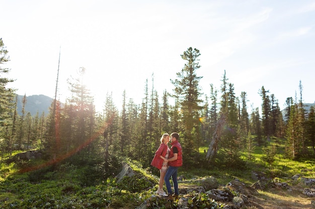 Belle jeune femme et homme marchent dans un câlin et s'embrassent dans la nature de la montagne au soleil