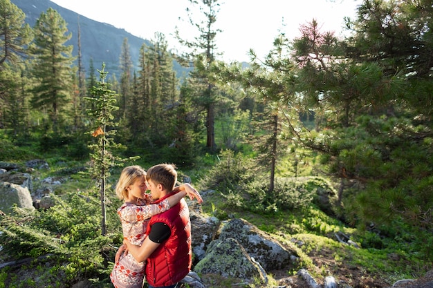 Belle jeune femme et homme marchent dans un câlin et s'embrassent dans la nature de la montagne au soleil