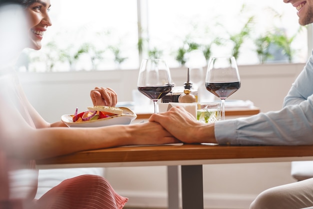 Belle jeune femme et homme se tenant la main et souriant tout en étant assis à table avec de délicieux plats et vins