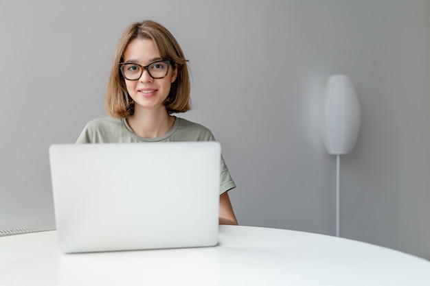 Belle jeune femme indépendante à l'aide d'un ordinateur portable assis à la table de bureau