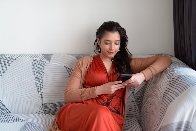 Belle jeune femme indienne à l'aide de téléphone dans le salon à la maison