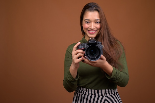 Belle jeune femme indienne avec appareil photo contre le mur marron