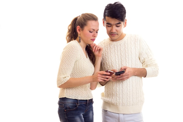 Belle jeune femme avec un jeune homme aux cheveux noirs en pulls blancs et jeans à l'aide d'un smartphone