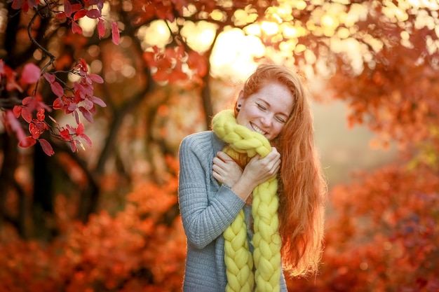 Une belle jeune femme joyeuse se tient dans la forêt sur fond d'arbres d'automne rouge