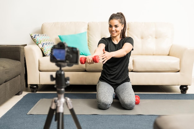 Belle jeune femme latine soulevant des poids et montrant la bonne technique sur son blog vidéo de fitness