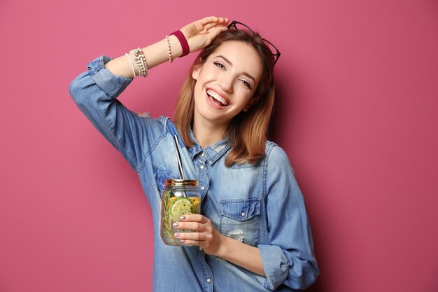 Belle jeune femme avec de la limonade sur fond de couleur