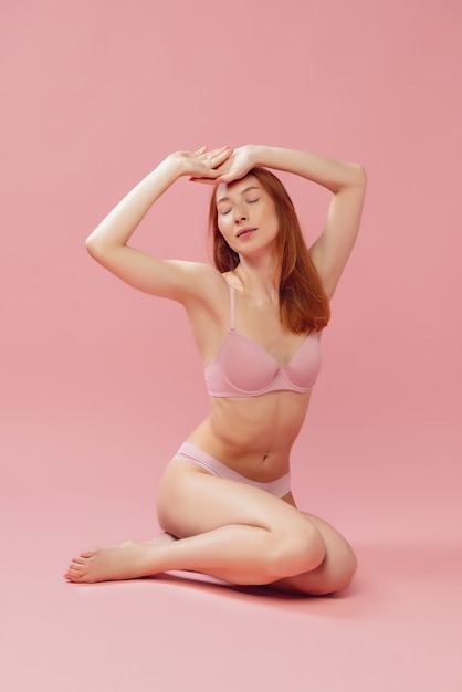 Belle jeune femme en lingerie posant isolée sur la beauté naturelle du mur du studio rose