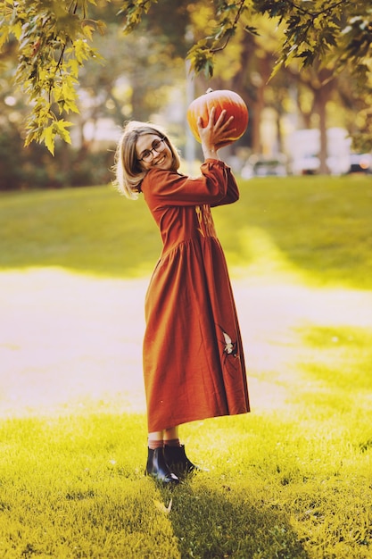 Belle jeune femme a un loisir debout avec de la citrouille dans les mains dans le parc d'automne