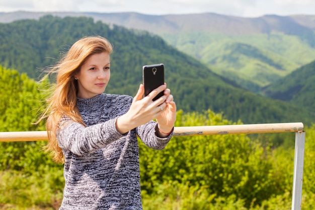 La belle jeune femme avec de longs cheveux fait le selfie à son téléphone sur le fond de la nature verte