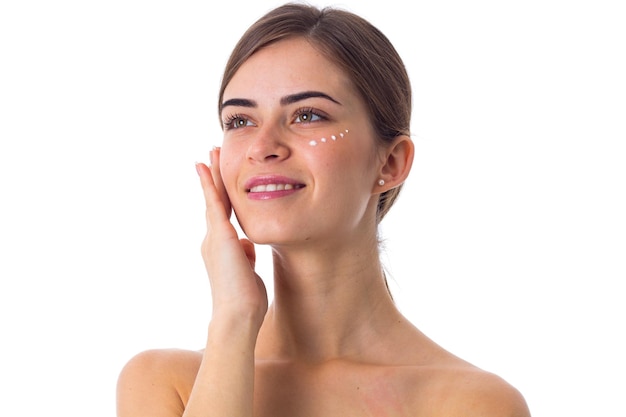 Belle jeune femme avec une longue queue de cheval brune et des points de crème sur son visage en studio