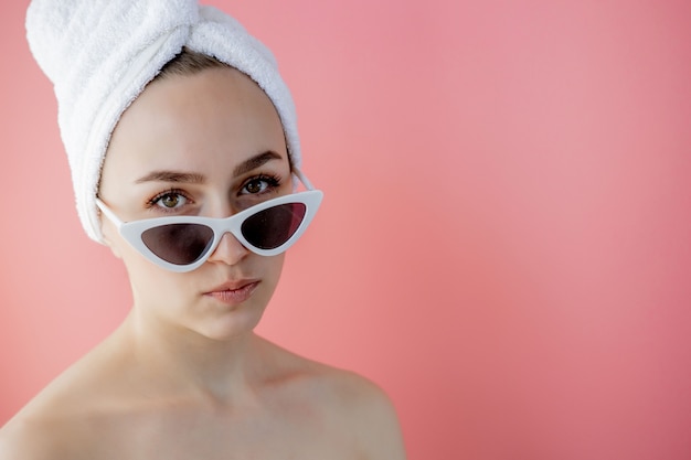 Belle jeune femme à lunettes avec une serviette sur la tête après le bain sur rose