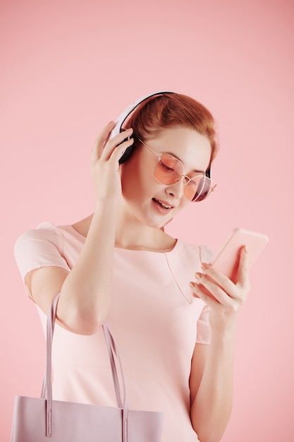 Belle jeune femme à lunettes de soleil choisissant la chanson à écouter au casque via une application sur smartphone