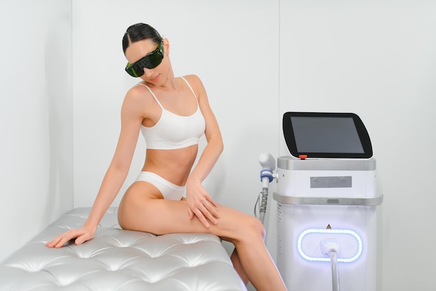 Une belle jeune femme avec une machine d'épilation au laser dans le cabinet de cosmétique