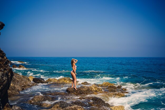 Belle jeune femme en maillot de bain sur une plage rocheuse par une journée ensoleillée sur fond de vagues Vacances en été Mise au point sélective