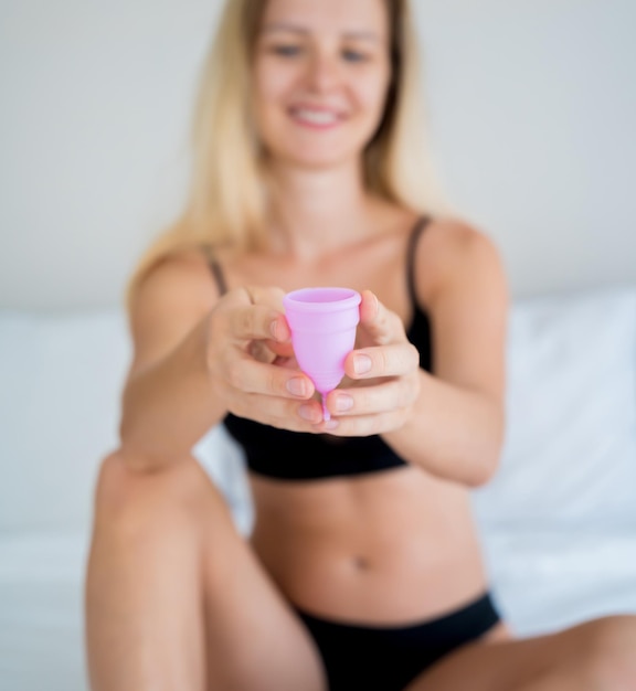 Belle jeune femme à la maison tenant une coupe menstruelle dans ses mains