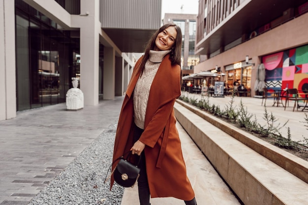 Une belle jeune femme en manteau brun marche dans la rue de l'automne