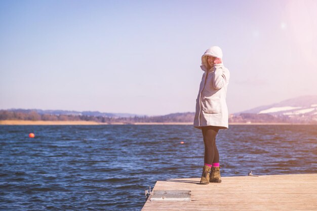 La belle jeune femme avec le manteau gris se tient sur une passerelle et apprécie le temps d'hiver de vue