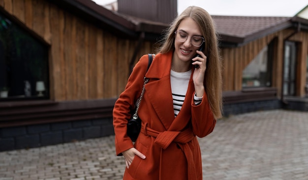 Belle jeune femme en manteau parlant sur un téléphone portable dans le contexte d'un immeuble de la ville