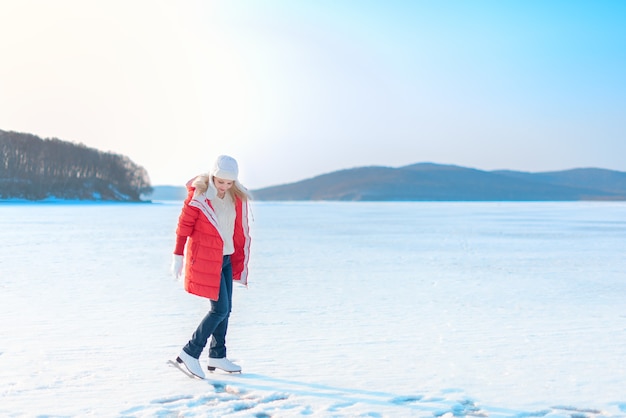 Belle jeune femme en manteau rouge et patins artistiques se dresse sur la mer gelée