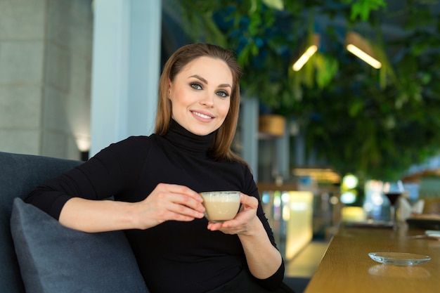 Belle jeune femme avec maquillage et coiffure avec une tasse de café à une table dans un restaurant