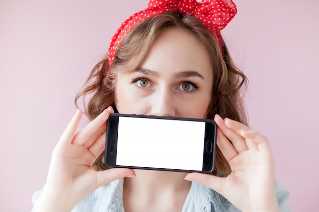 Belle jeune femme avec maquillage pin up et coiffure sur mur rose avec téléphone portable avec copie espace