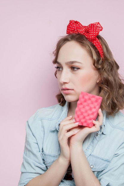 Belle jeune femme avec maquillage pin-up et coiffure avec des outils de nettoyage sur fond rose