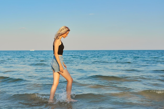 Belle jeune femme marchant de profil sur l'eau le long de la plage de la mer