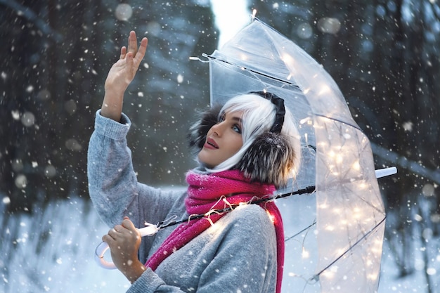 Belle jeune femme marchant sous un parapluie transparent au jour d'hiver enneigé