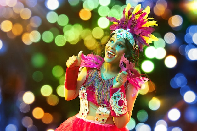 Belle jeune femme en masque de carnaval et costume de mascarade dans des lumières colorées