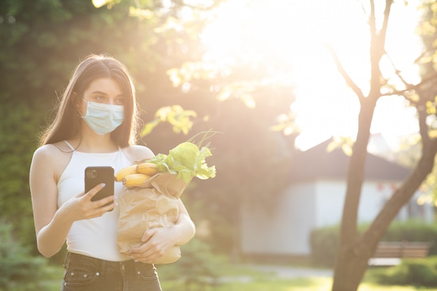 Belle jeune femme avec un masque dans le parc avec épicerie