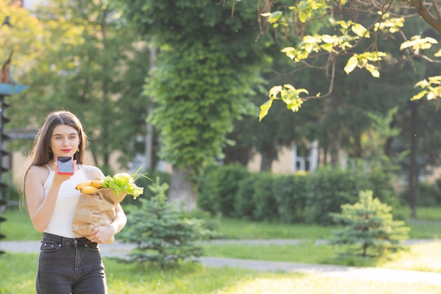 Belle jeune femme avec un masque dans le parc avec épicerie