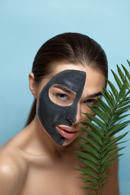 Belle jeune femme avec un masque pour le visage d'argile noire sur une peau propre et fraîche