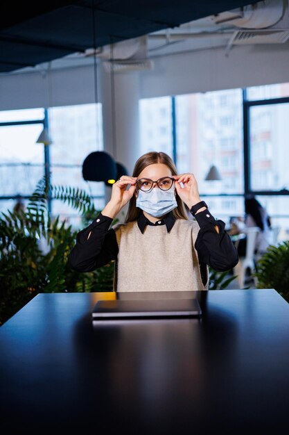 Belle jeune femme masquée travaillant dans un café avec un ordinateur portable pendant la pandémie de coronavirus