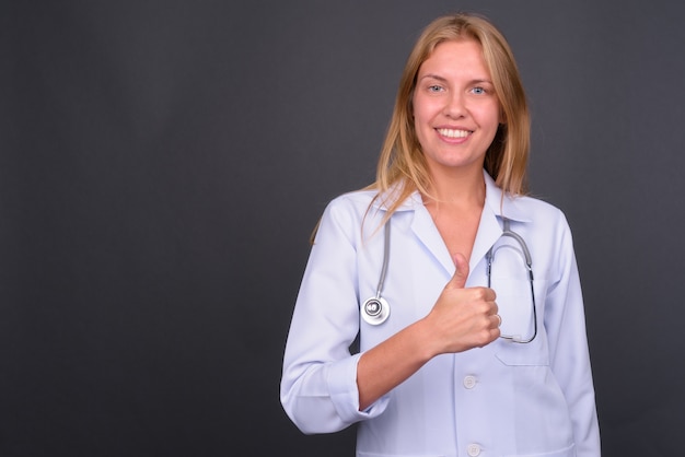 Belle jeune femme médecin aux cheveux blonds contre le mur gris