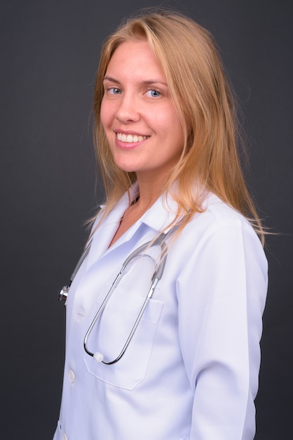 Belle jeune femme médecin aux cheveux blonds contre le mur gris