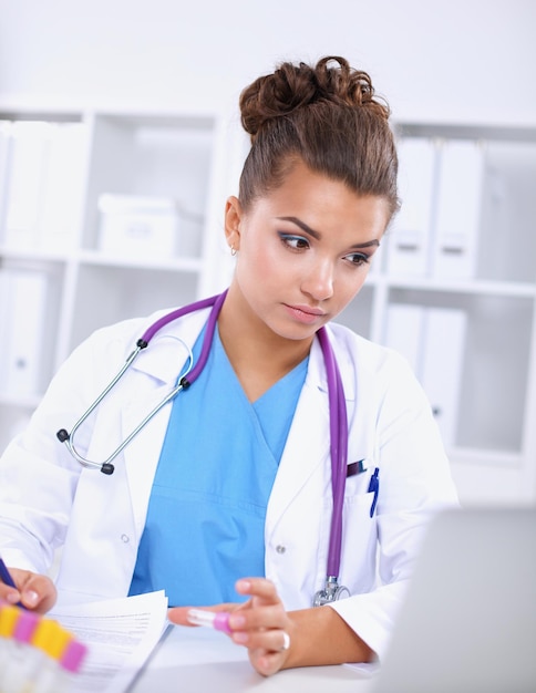 Belle jeune femme médecin souriante assise au bureau et écrivant.