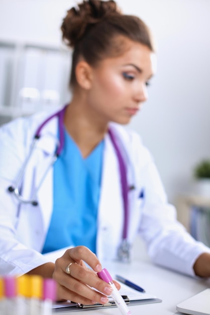 Belle jeune femme médecin souriante assise au bureau et écrivant.